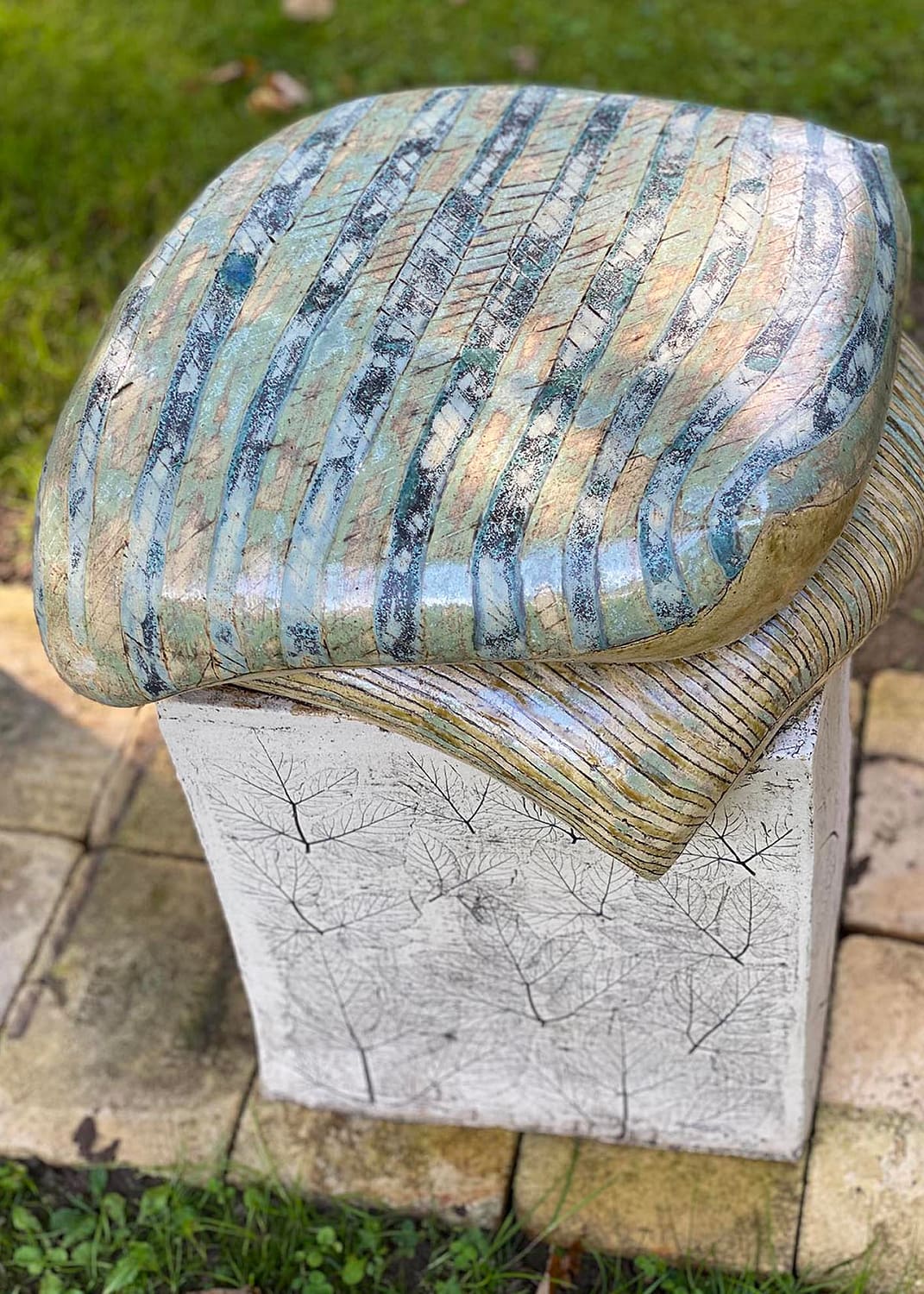Keramisk skulptur med 2 puder på en græsplæne med fliser